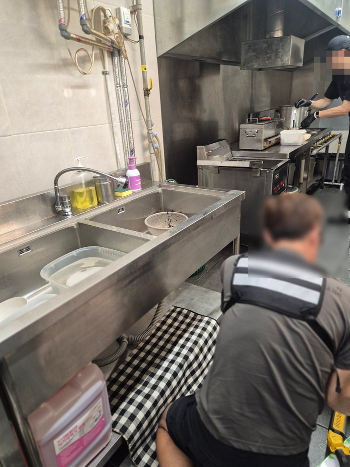 식당 싱크대 아래에서 배관을 손보는 작업 장면